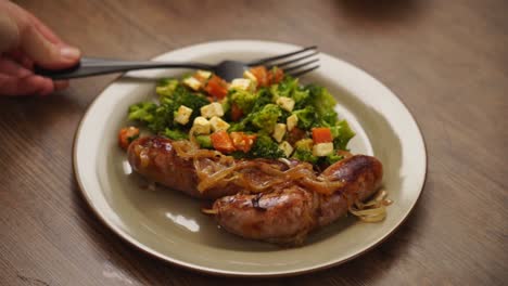 Crop-person-putting-fork-on-plate-with-salad-and-sausages
