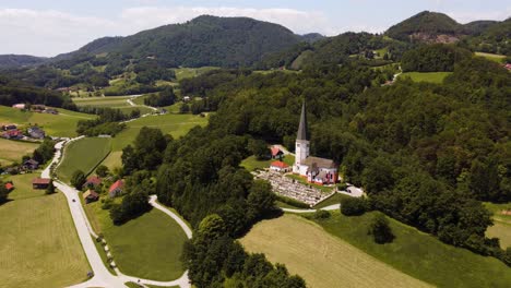 Aerial-birds-eye-shot-of-cemetery-with-church-tower-in-scenic-landscape-during-sunny-day-in-Olimje,-Slovenia