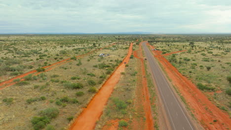 Pista-De-Carreras-De-Tierra-Roja-Con-Camiones-De-Trofeos-Corriendo-Junto-A-La-Autopista-En-La-Carrera-Del-Desierto-De-Finke,-4k-Drone-Australia