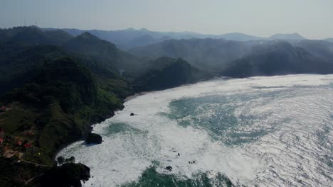 Filmische-Drohnenaufnahme-Riesiger-Meereswellen,-Die-Im-Sommer-Eine-Wunderschöne-Küste-Mit-Bergketten-Erreichen-–-Zentral-Java,-Indonesien-–-Einführung-Eines-Drohnenflugs