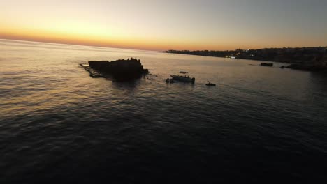 Aerial-fpv-flight-over-seascape-with-boats-and-people-on-rock-during-golden-Sunset---Batroun,-Lebanon