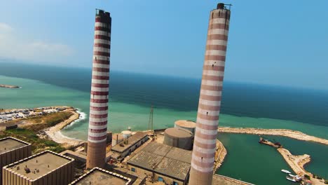 FPV-Flying-Between-Large-Columns-Of-Smoke-Pipe-Thermal-Power-Plant-On-Sunny-Day,-Zouk,-Lebanon