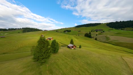 FPV-drone-flying-above-the-cabins-in-Alpe-di-Siusi,-Seiser-Alm-meadows-at-sunrise-in-the-Dolomite-mountains,-Italian-Alps
