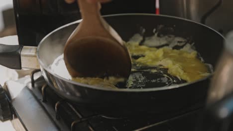 Close-Up-Shot-Of-Person-Frying-Eggs-Using-Big-Wooden-Spoon-In-Frying-Pan