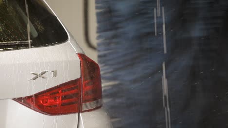 The-handheld-camera-tracks-a-white-BMW,-partially-veiled-in-soap-suds,-navigating-its-way-through-a-car-wash,-set-against-an-array-of-blue-bristles-and-cascading-water-droplets