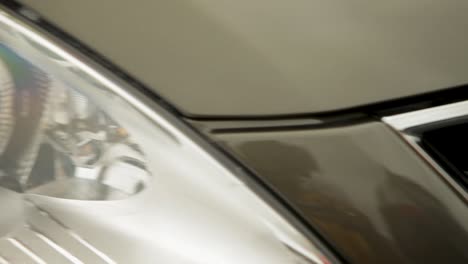 In-a-subtle-camera-pan,-a-close-up-captures-the-round-car-headlight-with-a-silver-metallic-finish,-slightly-blurred-against-a-completely-blurred-light-colored-car-body-backdrop