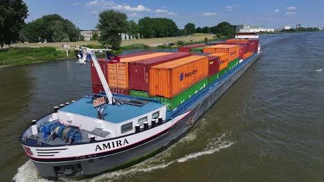 Container-ship-"AMIRA"-sails-along-Dutch-river-past-Zwijndrecht's-sunny-banks-on-a-summer-day