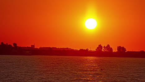 Zeitraffer-Eines-Roten,-Warmen-Sonnenaufgangs-An-Einem-See-Mit-Bäumen-Im-Hintergrund