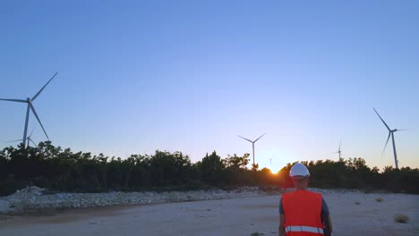 Aerial-view-following-engineer-walking-toward-wind-power-turbine-at-a-Eolic-farm