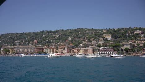 Ferry-Navegando-Y-Navegando-Por-El-Mar-De-Liguria-En-Portofino,-Italia-Y-Con-La-Vista-De-Fondo-De-Las-Vibrantes-Casas-Y-Barcos