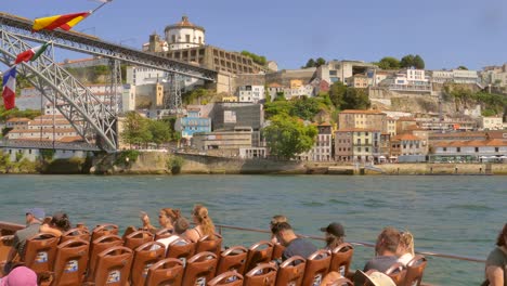 Turistas-En-Excursión-En-Barco-Mirando-El-Icónico-Puente-De-Dom-Luis-Sobre-El-Río-Duero-Y-Vila-Nova-De-Gaia-En-Porto,-Portugal