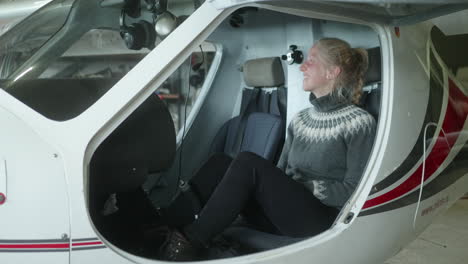 Close-up-of-A-Pretty-Blond-Nordic-Girl-Sitting-in-a-Sports-Aircraft,-Propeller-Plane-in-the-Hangar