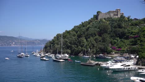 Castello-Brown,-Un-Castillo-Histórico-Encaramado-Sobre-Una-Colina-Que-Domina-El-Pueblo-Y-Barcos-Navegando-Y-Amarrando-En-El-Pequeño-Puerto-De-Portofino,-Italia