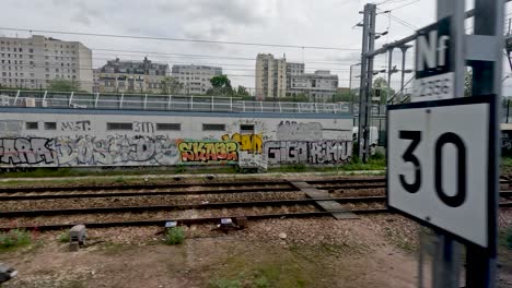 Looking-out-of-the-window-of-an-SNCF-train-traveling-through-Paris-passing-buildings-covered-in-graffiti,-France