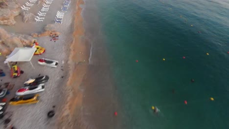 FPV-Flug-Entlang-Sandstrand-Und-Klarem-Wasser-Mit-Schwimmenden-Menschen-Während-Des-Sonnenuntergangs-Im-Libanon
