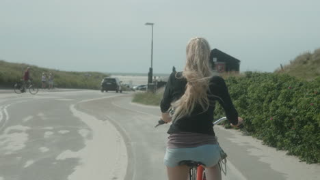 Hübsche-Blonde-Frau,-Die-An-Einem-Sonnigen-Sommertag-In-Dänemark,-Fanø-Strand,-Esbjerg,-Mit-Dem-Fahrrad-Zum-Strand-Fährt