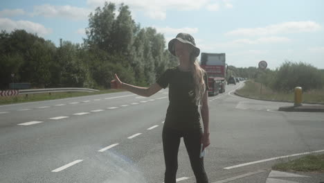 Young-Female-Hitchhiker-Standing-on-the-Side-of-the-Road-Waiting-for-a-Car-to-Stop,-A-lot-of-Cars-Are-Passing-By,-Traffic-in-Denmark