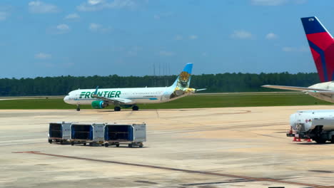 Frontier-Airlines-jet-taxing-on-runway-and-baggage-train-pulling-up-to-plane