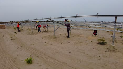 Técnicos-Ocupados-Ensamblando-Marcos-Y-Estructuras-De-Paneles-Solares-Fotovoltaicos-En-Un-Proyecto-De-Granja-Solar-En-Gambia,-África-Occidental