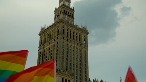 Ondeando-Banderas-Del-Arco-Iris-Y-La-Torre-Del-Reloj-Del-Palacio-De-La-Cultura-Y-La-Ciencia-Contra-El-Cielo-Dramático-En-Varsovia,-Polonia