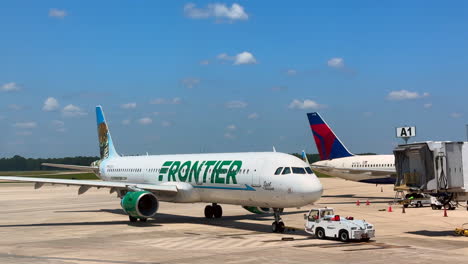Frontier-Airlines-plane-being-pushed-away-from-sky-bridge-terminal-at-airport