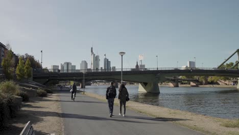 Tourists-taking-a-walk-next-to-river-main-with-beautiful-Frankfurt-skyline