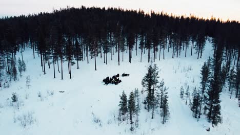 drone-shot-of-a-group-of-people-standing-on-top-of-a-mountain-with-snowmobiles-during-sunset