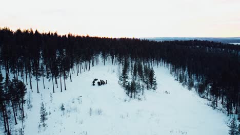 drone-shot-of-a-group-of-people-standing-on-top-of-a-mountain-with-snowmobiles-during-sunset-from-the-distance