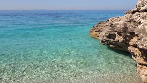 Beautiful-shore-with-big-rocks,-pebble,-and-shallow-turquoise-sea-water-on-a-hot-summer-vacation-day-in-Mediterranean