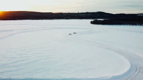 drone-shot-of-two-sports-cars-driving-on-a-frozen-lake-during-sunset