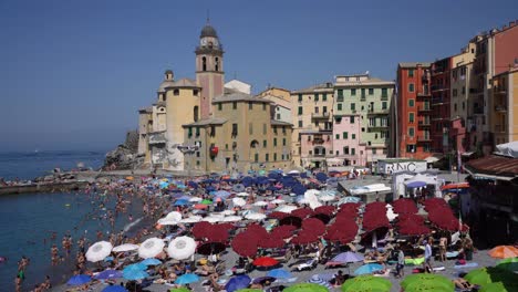 Ikonischer-Blick-Auf-Die-Berühmte-Basilika-Der-Kirche-Santa-Maria-Assunta,-Touristen-Sonnen-Sich,-Spielen-Wasseraktivitäten-Und-Genießen-Die-Warme-Mediterrane-Sonne-In-Camogli,-Italien