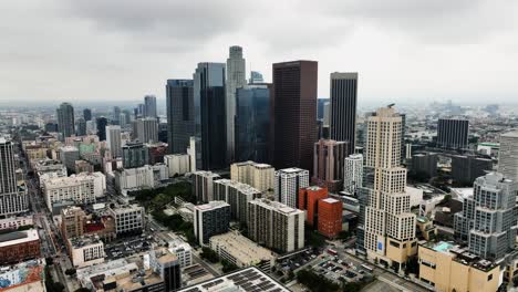 Drone-shot-circling-the-corporate-skyline-of-LA-city,-dark,-overcast-day-in-USA