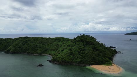 Picturesque-small-wooded-island-in-the-tropical-ocean-with-sand-beach,-aerial