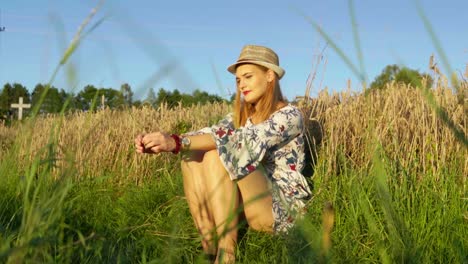 Stunning-HD-footage-of-a-white-caucasian-girl-in-a-dress-with-a-knitted-hat-and-red-lipstick-sitting-in-a-wheat-field,-lost-in-thought,-basking-in-the-setting-sun's-warm-embrace