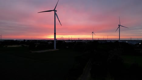 Silhouette-of-wind-turbines-against-red-sunset-sky,-aerial-ascend-view