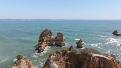 Ridgeline-leads-out-to-oceanic-arch-battered-by-ocean-waves-crashing,-lagos-algarve-portugal