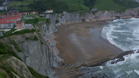 Epic-cliffside-beach-of-Itzurun,-aerial-rising-dolly-above-strong-crashing-waves