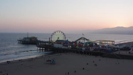 Low-aerial-push-in-shot-of-the-busy-Santa-Monica-Pier-on-a-warm-summer-night-in-Southern-California-at-twilight