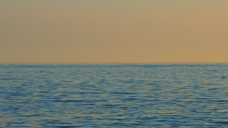 Calm-ocean-waves-during-sundown-with-clear-orange-sky