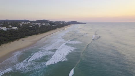 Sandy-Coastline-Of-Sunshine-Beach-During-Sunrise-With-Surfers-In-Queensland,-Australia