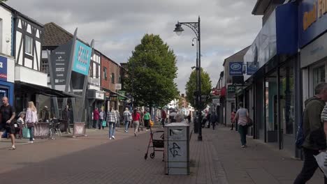 Slow-motion-people-walking-across-British-Widnes-town-main-street-passing-shops-during-cost-of-living-crisis-recession