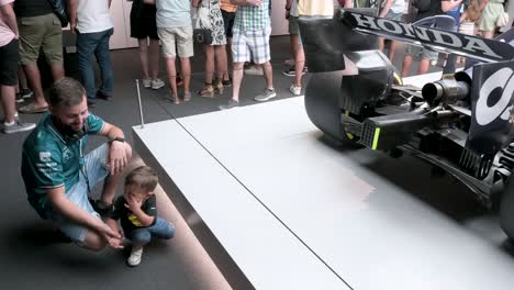 A-father-and-his-son-are-seen-next-to-the-F1-car-racing-Lotus-49,-Alpha-Tauri,-during-the-world's-first-official-Formula-1-exhibition-at-IFEMA-Madrid,-Spain