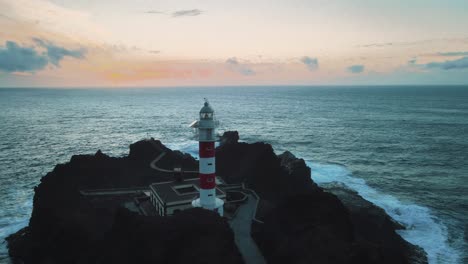 Aerial-Pan-Around-Old-Historic-White-Lighthouse-by-the-Bright-Blue-Ocean,-Costal-Spain