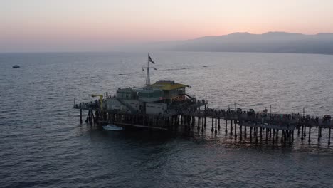 Aerial-close-up-panning-shot-of-the-restaurant-at-the-end-of-the-Santa-Monica-Pier-on-a-busy-summer-night-at-twilight