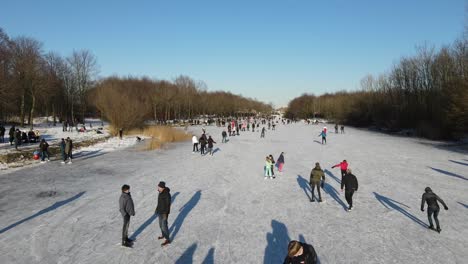 Drone-filming-a-large-group-of-people-skating-on-natural-ice-on-a-sunny-day
