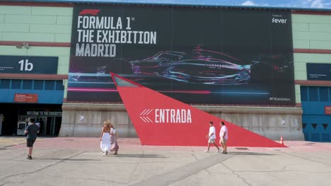 Visitors-walk-past-a-large-banner-as-they-arrive-at-the-world's-first-official-Formula-1-exhibition-in-Madrid,-Spain