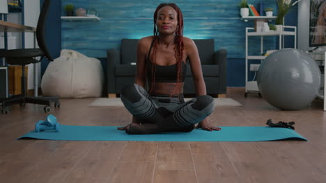 Athlete-slim-woman-with-dark-skin-getting-in-lotus-position-on-yoga-map