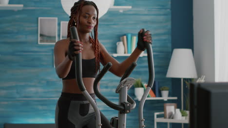 Fit-athletic-black-woman-running-on-elliptical-bike-watching-wellness-routine