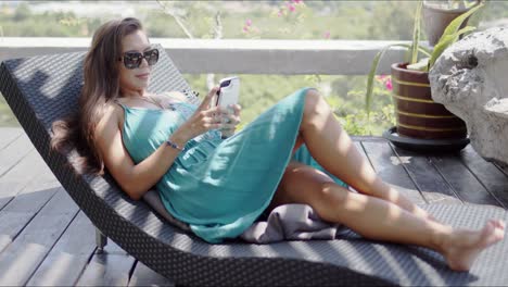 Attractive-woman-with-smartphone-resting-on-chaise-lounge