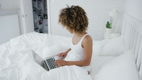 Pretty-woman-lounging-on-bed-with-laptop